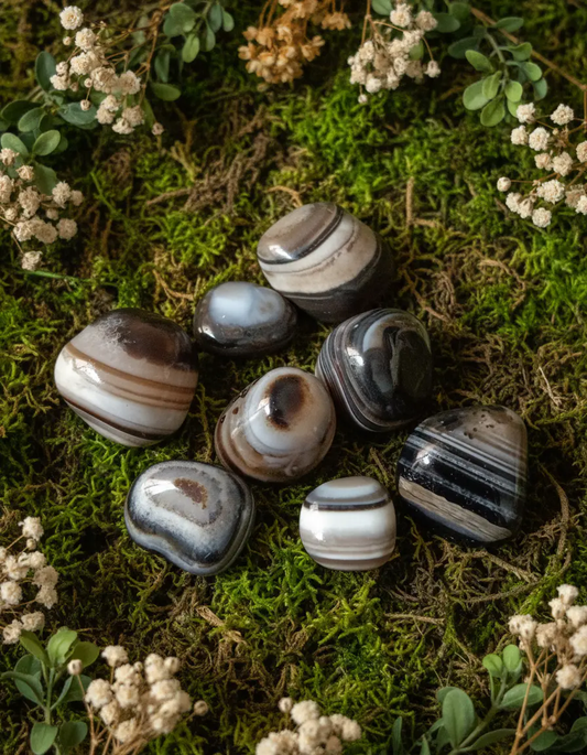 Smooth black banded agate tumbled stone displaying natural sulemani patterns on a neutral backdrop.