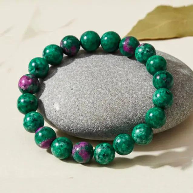 Ruby zoisite fertility bracelet with red and green crystal beads displayed on a neutral background.